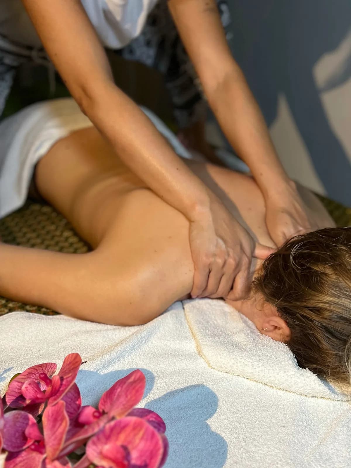 Mani della terapista che massaggiano olio caldo su spalle e collo della cliente a lume di candela durante un Massaggio Thailandese con Olio